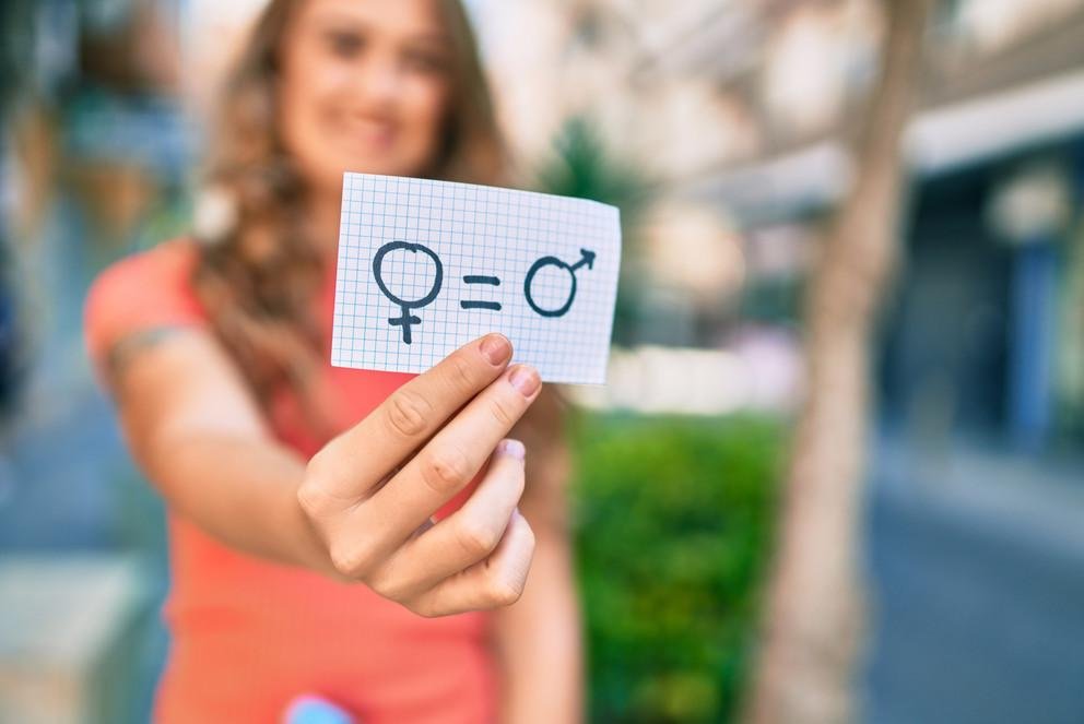 Symbolic image: A woman, who can only be seen in the background, holds up a piece of paper with a symbol for gender equality. 